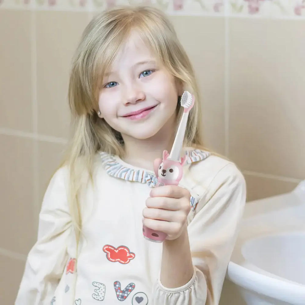 Pink kids electric toothbrush with deer handle held by smiling girl in bathroom