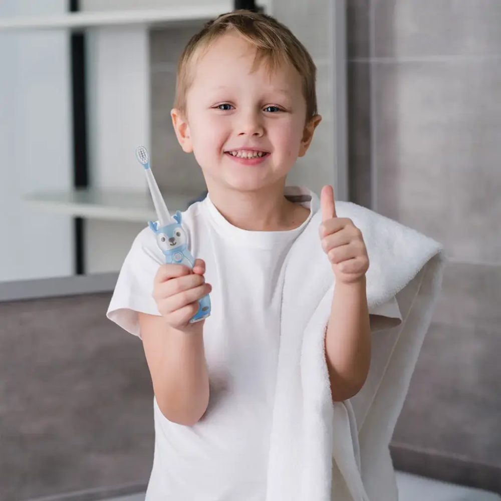 Blue kids electric toothbrush with deer handle held by boy giving thumbs up in bathroom