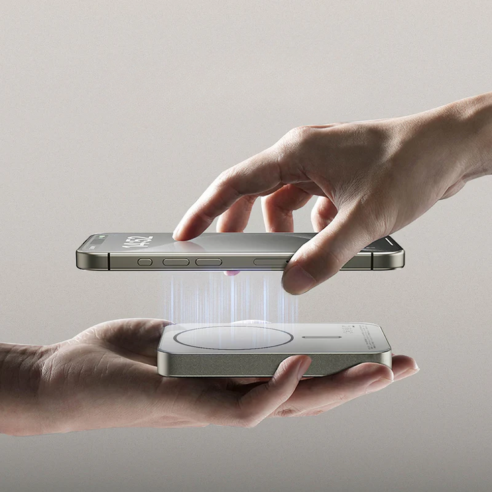 Hands demonstrating magnetic snap-on attachment of silver Momax power bank for fast wireless charging
