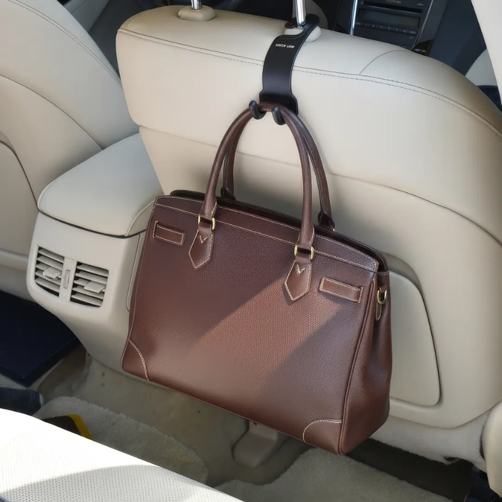 Black car headrest hook holding leather handbag on beige seat