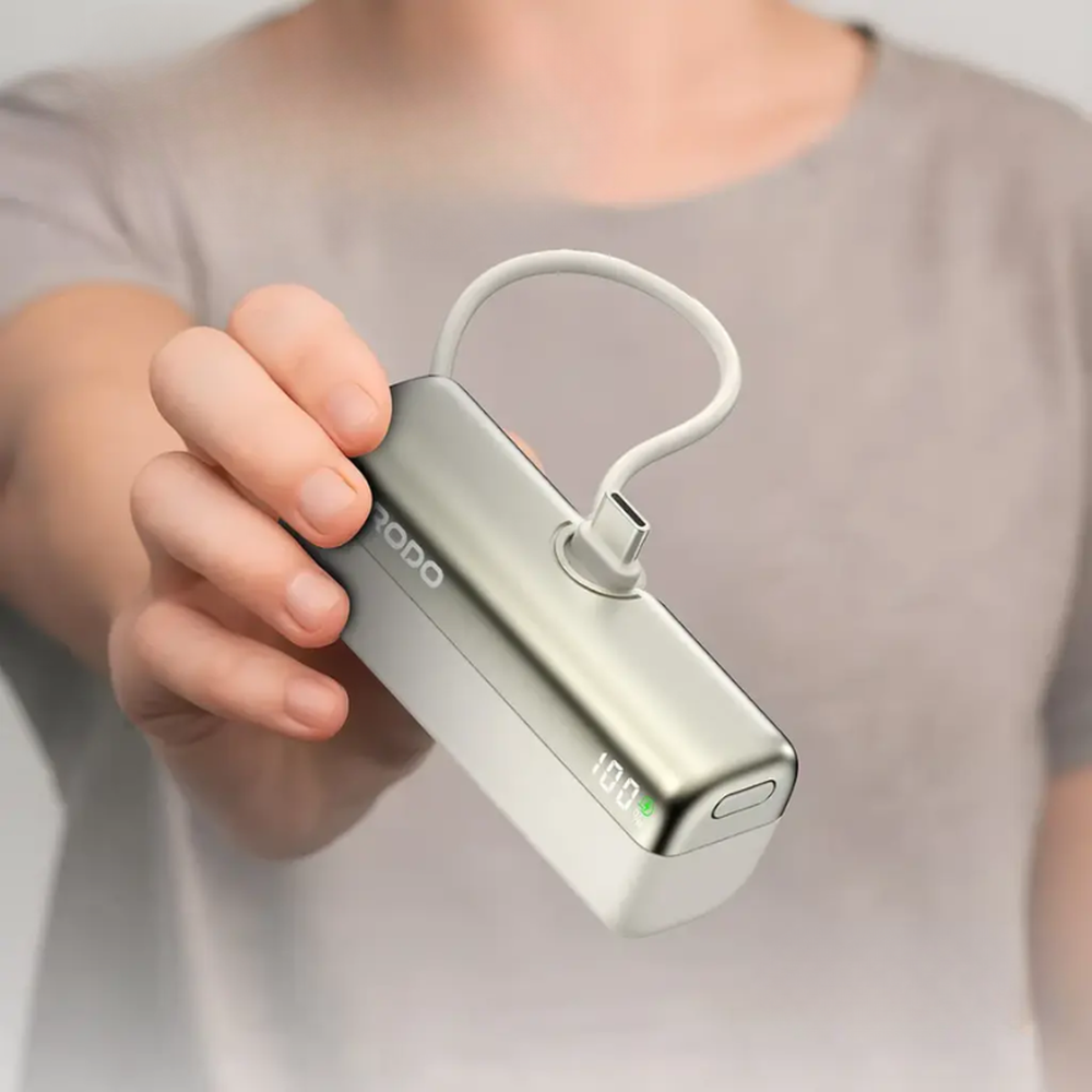 Hand holding Porodo 5000mAh power bank with digital display showing 100%