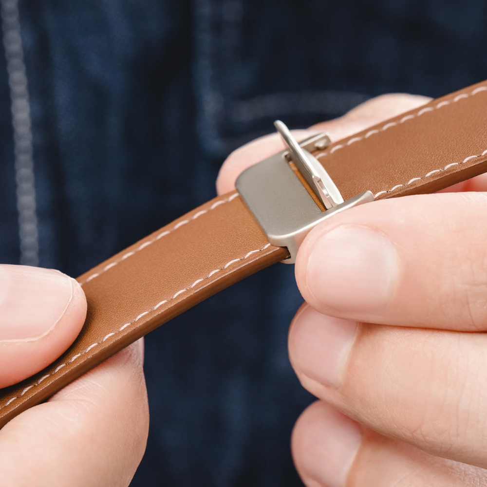 Hands snapping magnetic clasp onto brown leather Apple Watch band