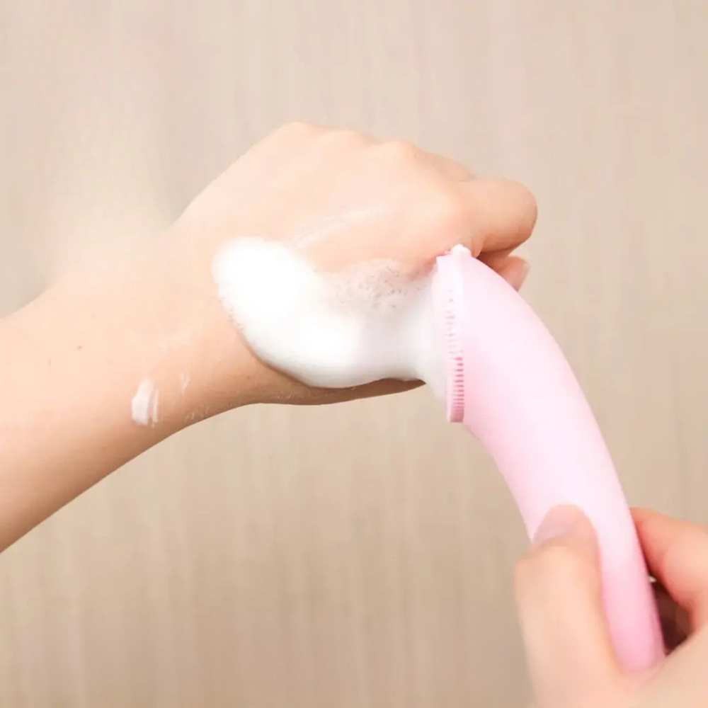 Pink sonic facial cleansing brush creating lather on hand