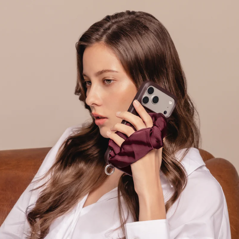 Maroon silk scarf phone case worn on fingers by woman in white shirt