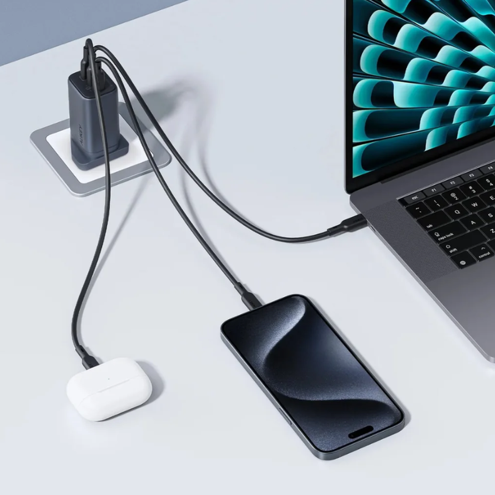 Aukey 3-port wall charger powering laptop and smartphone simultaneously on desk