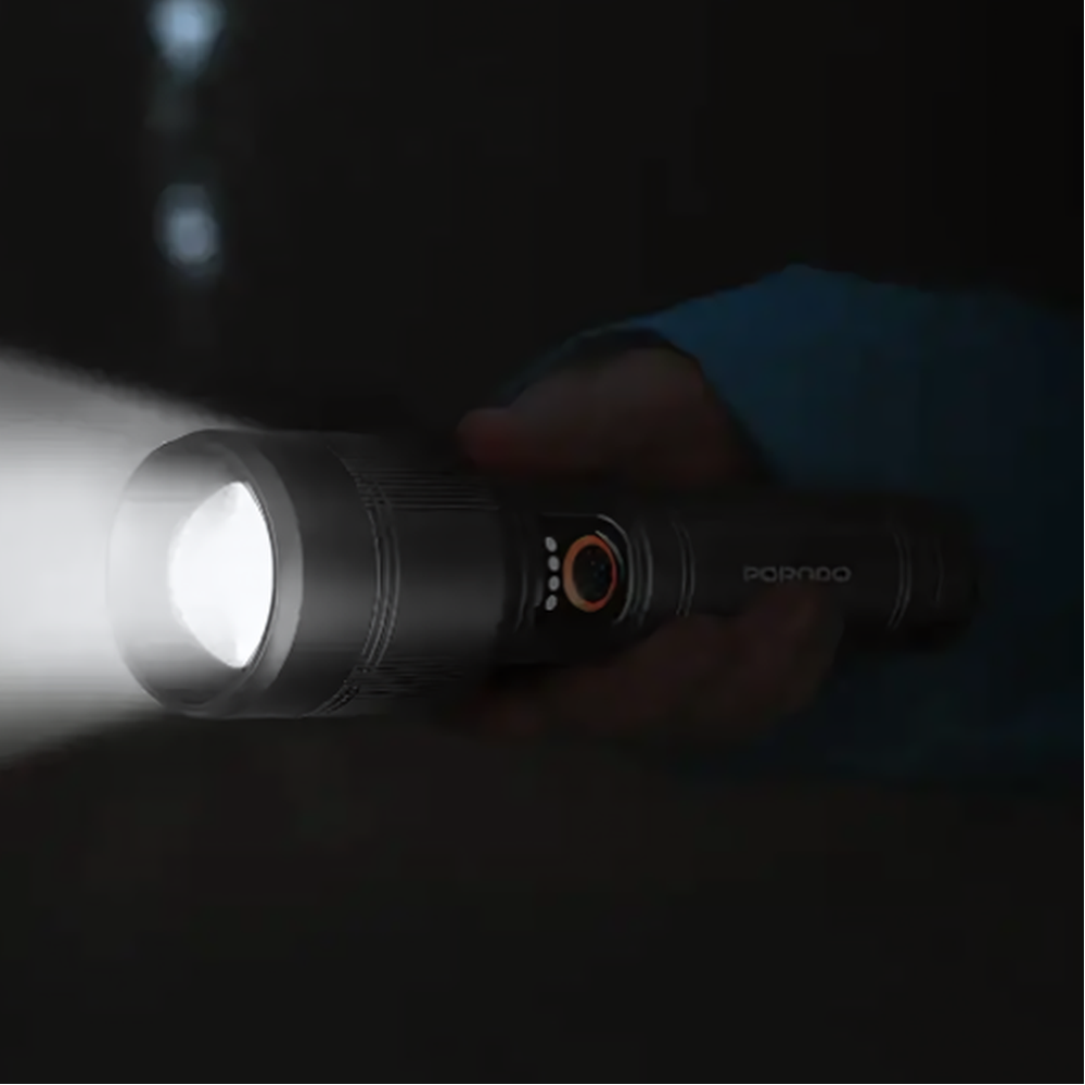 Hand holding black Porodo LED flashlight emitting bright beam in dark environment
