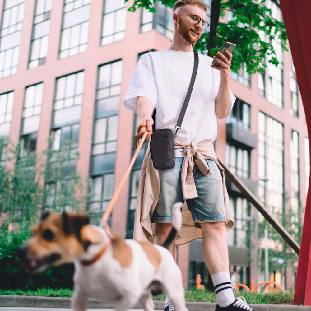 Man wearing black Spigen crossbody bag while walking dog outdoors