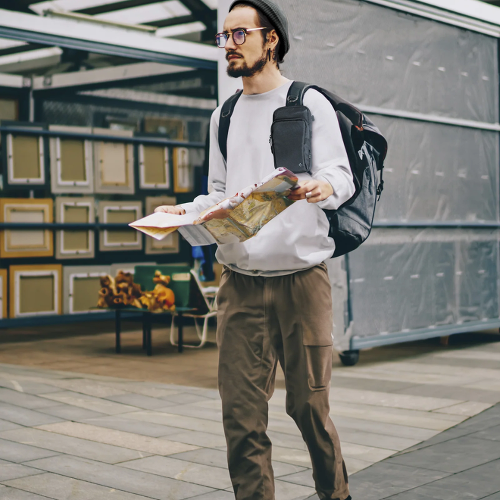 Traveler wearing black Spigen crossbody bag clipped to backpack