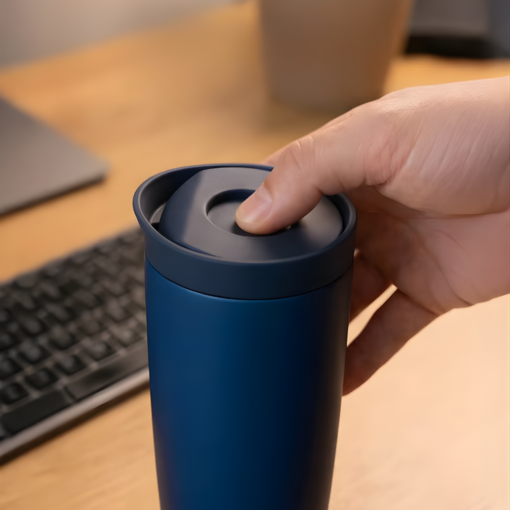 Hand pressing Brave navy blue travel mug lid at office desk