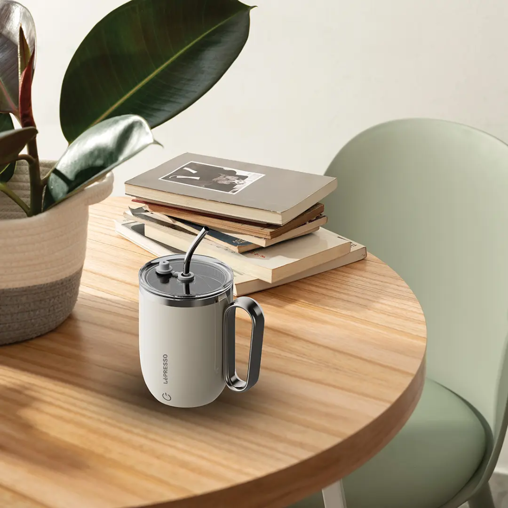 Beige Lepresso insulated coffee mug in home setting with plant