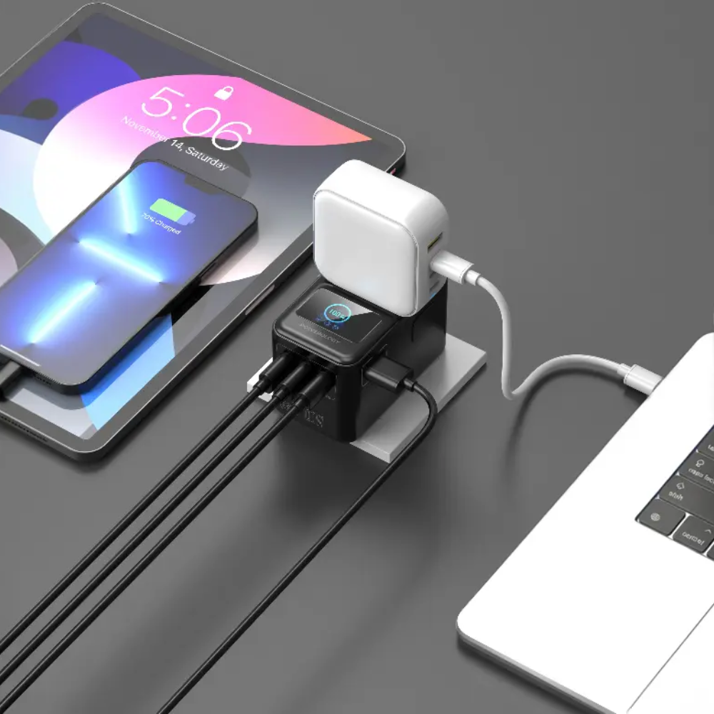 Black 100W travel adapter charging laptop and phone on desk with smart power monitor