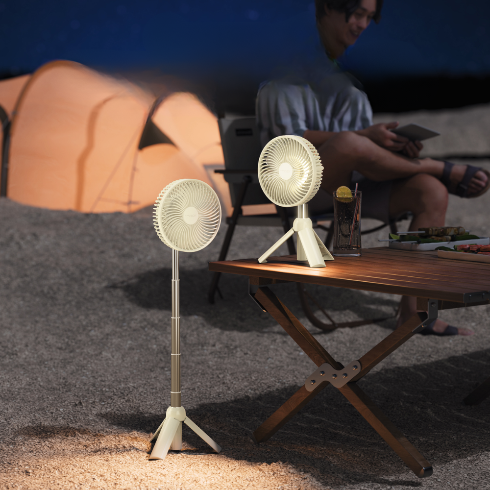 White tripod camping fan with LED light on wooden table at night beside tent