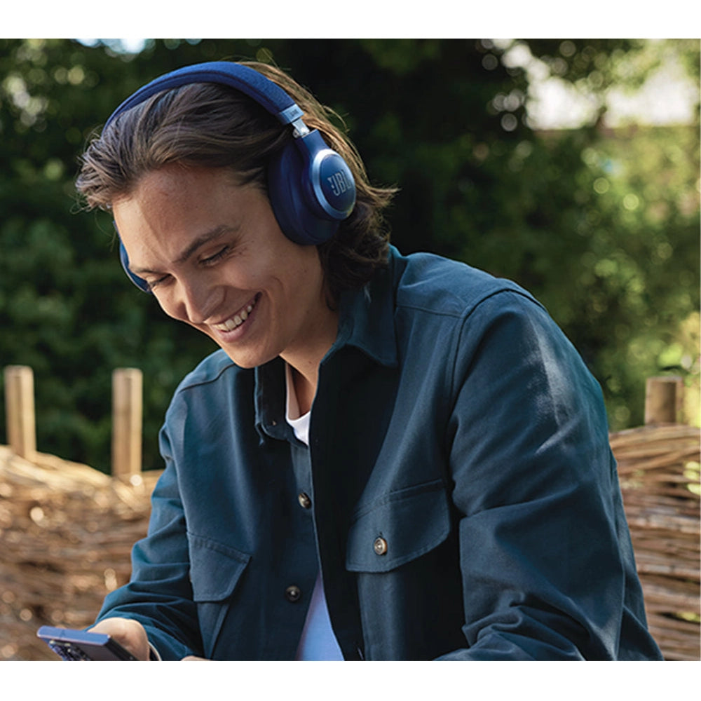 Man wearing blue JBL wireless headphones smiling while checking phone outside