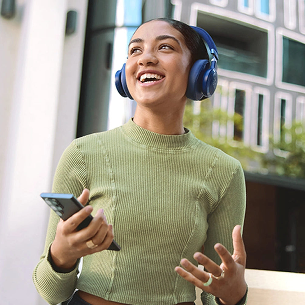 Woman wearing blue JBL wireless headphones outdoors while using smartphone