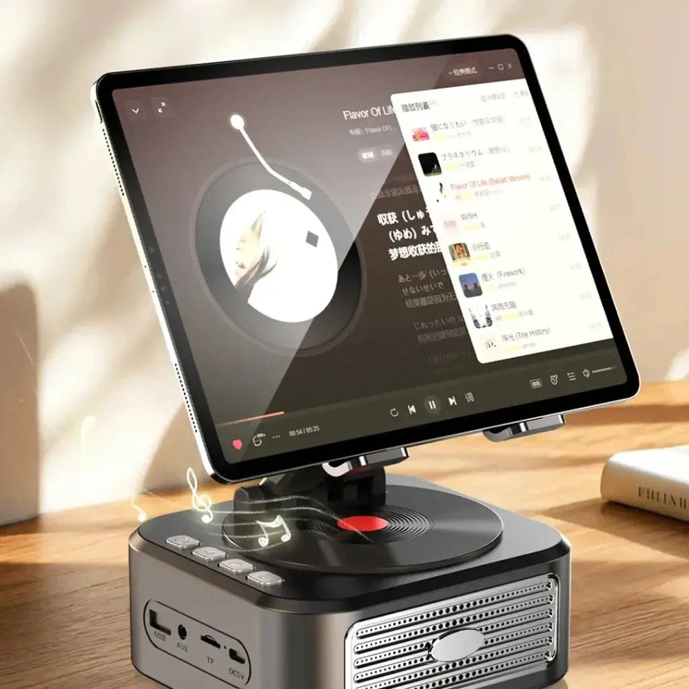 Black turntable-style tablet stand with silver speaker grille and USB AUX ports playing music