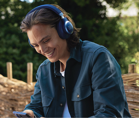 Man wearing blue headphones and a blue jacket, looking at his phone with a smile outdoors.